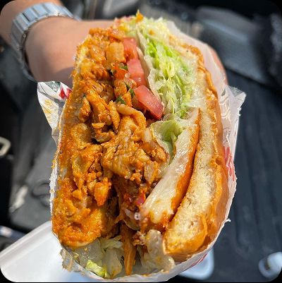 Customer holding a large, messy Mexican Torta sandwich cut open, showing the inside layers of chicken carnitas, fresh lettuce, tomato, and sauce.
